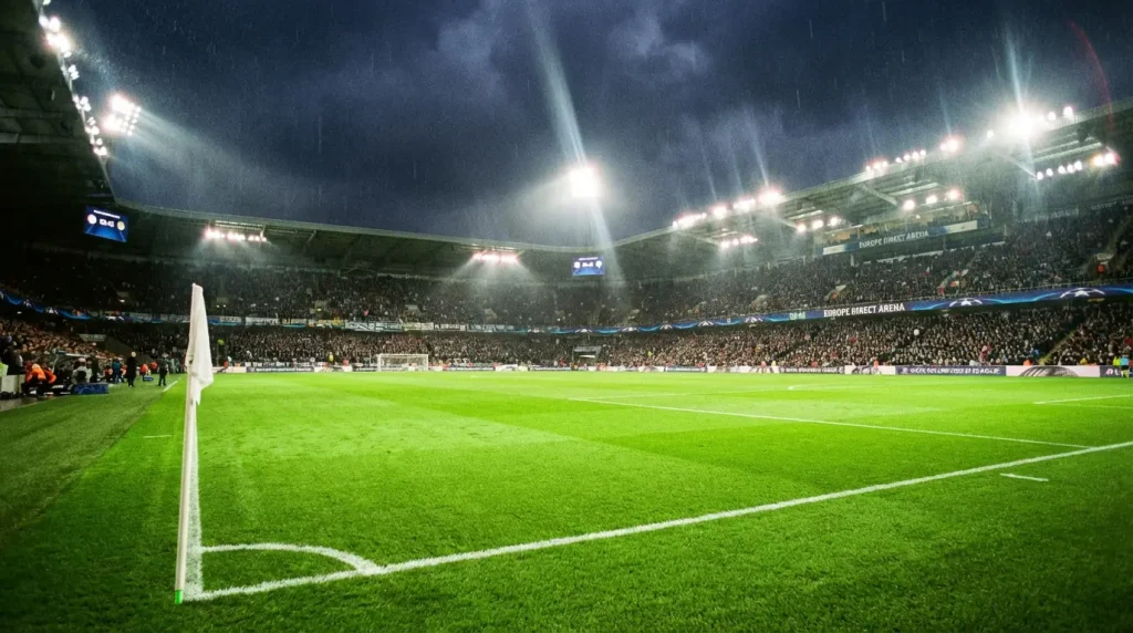 Stadio di calcio europeo illuminato di notte con campo verde e riflettori accesi